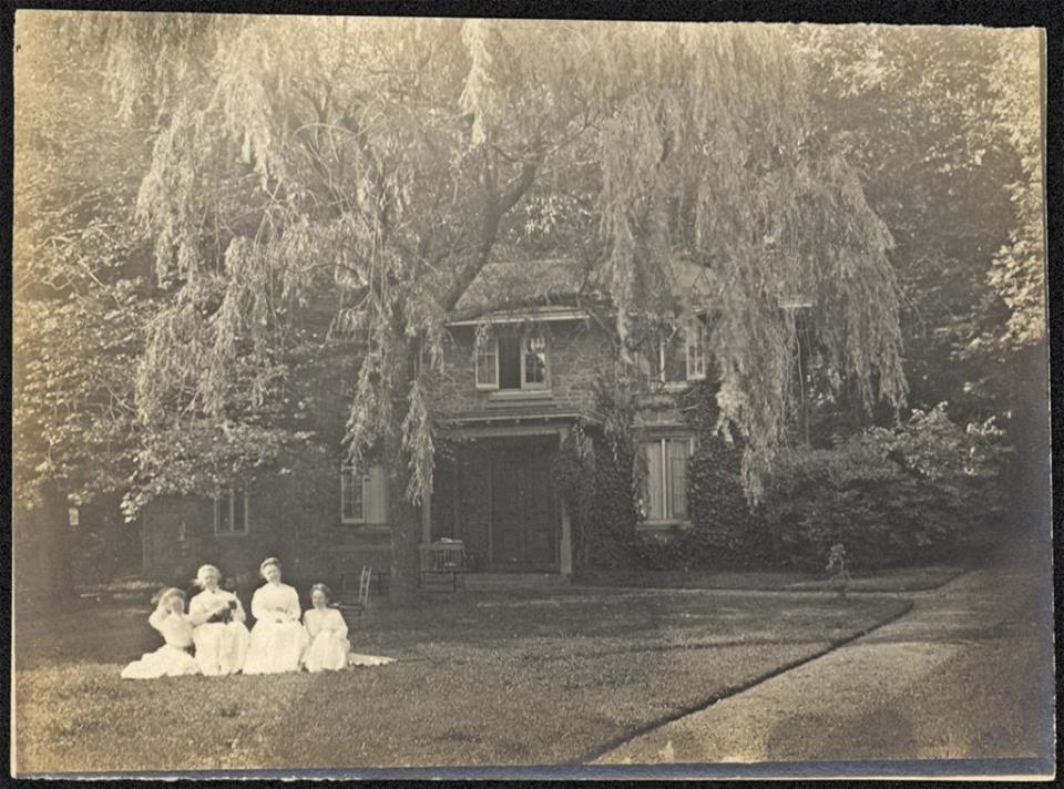 Vintage image of a group of girls sitting on the ground in front of a house.